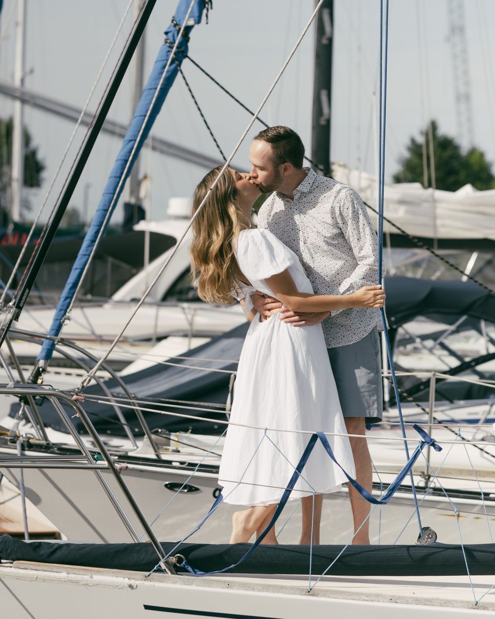 Two people in light summer clothing share an intimate moment on a sailboat deck.