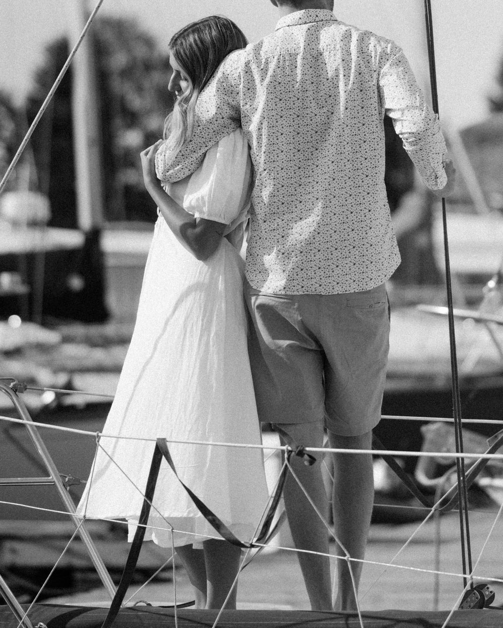 Black and white photo of a couple standing close together on a sailboat deck.