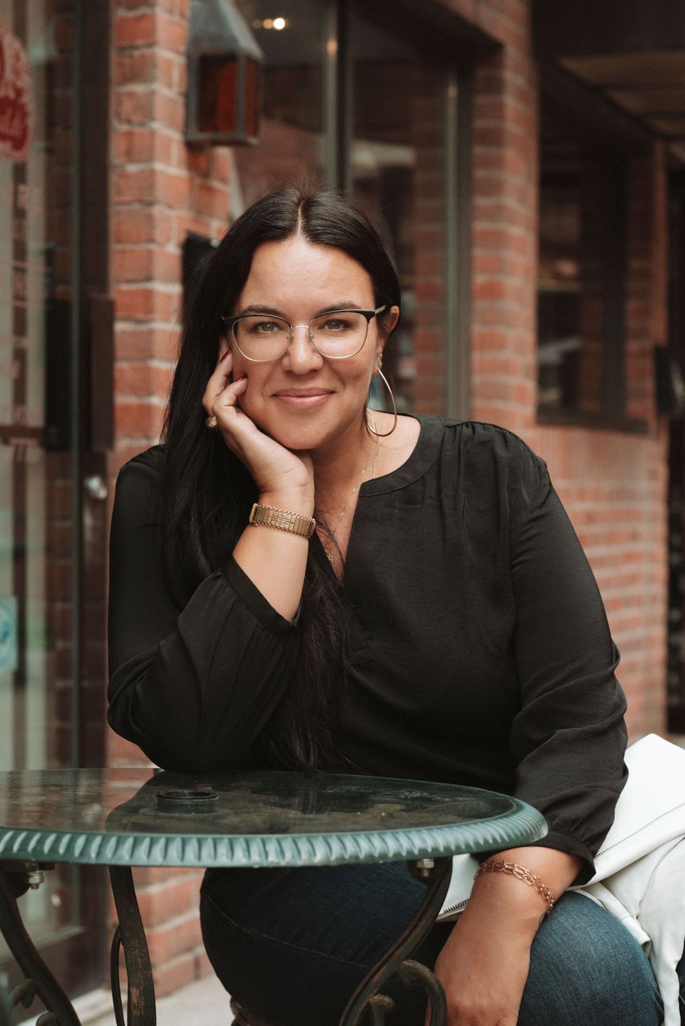 Stylish portrait at cafe table showing glasses and black top against brick wall background.