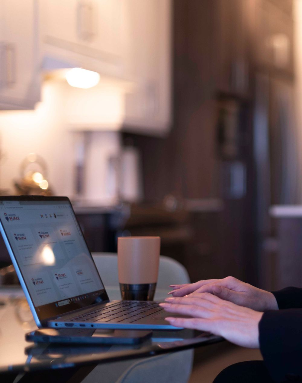 Person typing on laptop with coffee cup in dimly lit room.