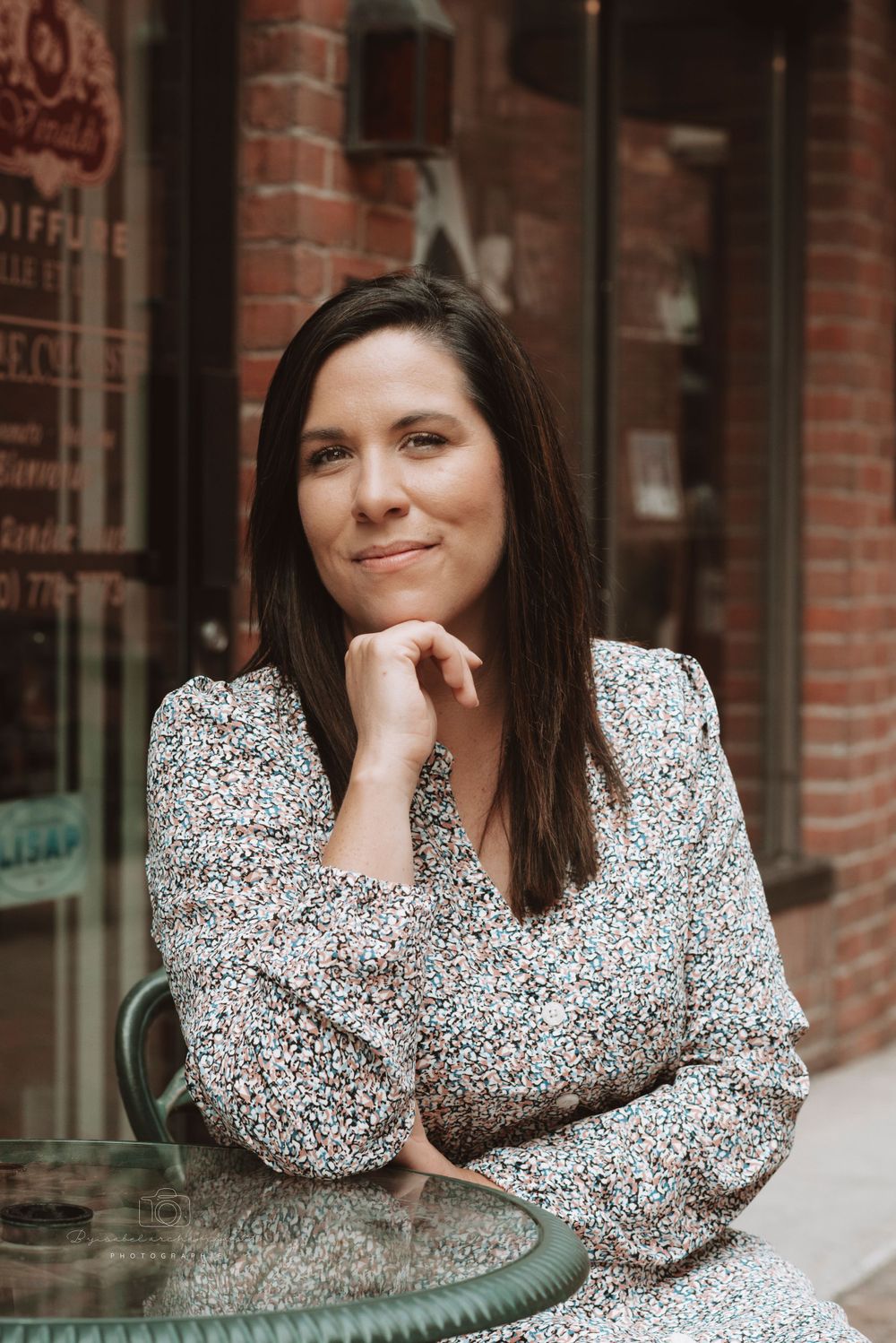 Business casual portrait against brick storefront with floral print dress.