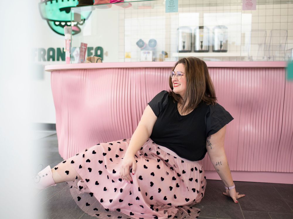 Someone in a polka dot skirt sits on a floor near a pink booth inside a retro-style diner or cafe.