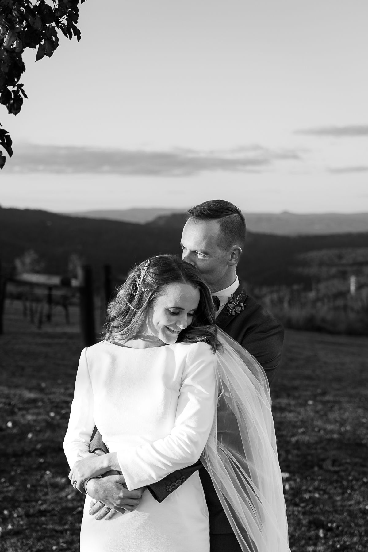 A couple embracing outdoors with a scenic landscape in the background. The image is in black and white.
