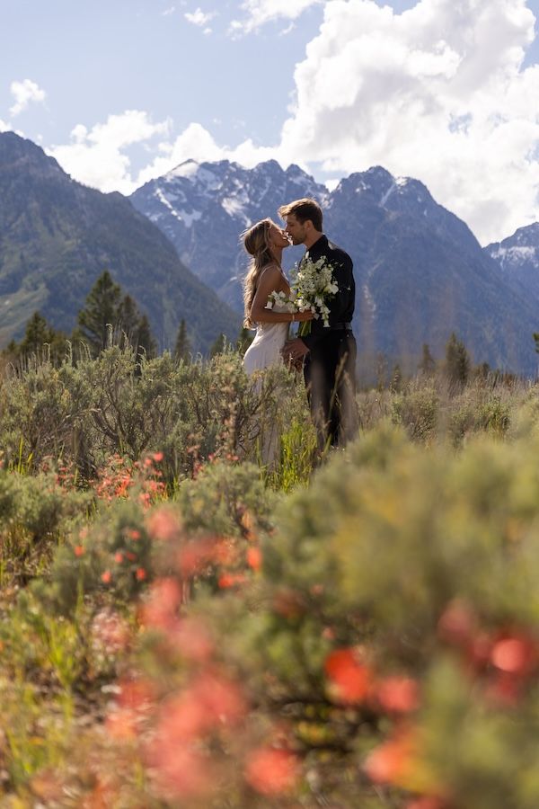 Couple kissing in wildflower meadow with snow-capped Grand Teton mountains backdrop on their wedding day.