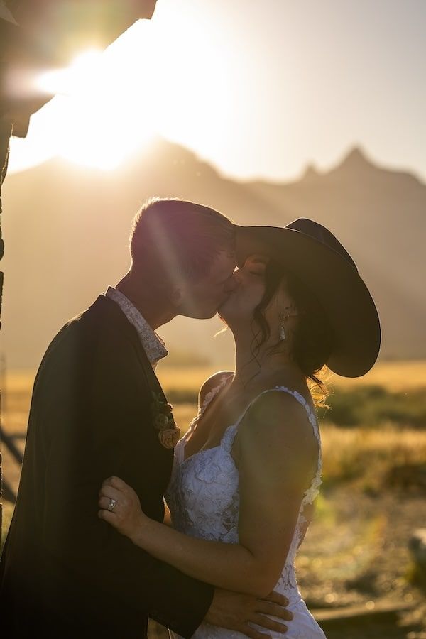 Silhouetted couple shares romantic kiss during a golden sunset in a rustic outdoor setting.