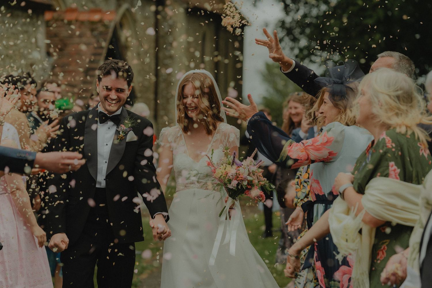 A dramatic wedding photo with flowing veil against an overcast sky.