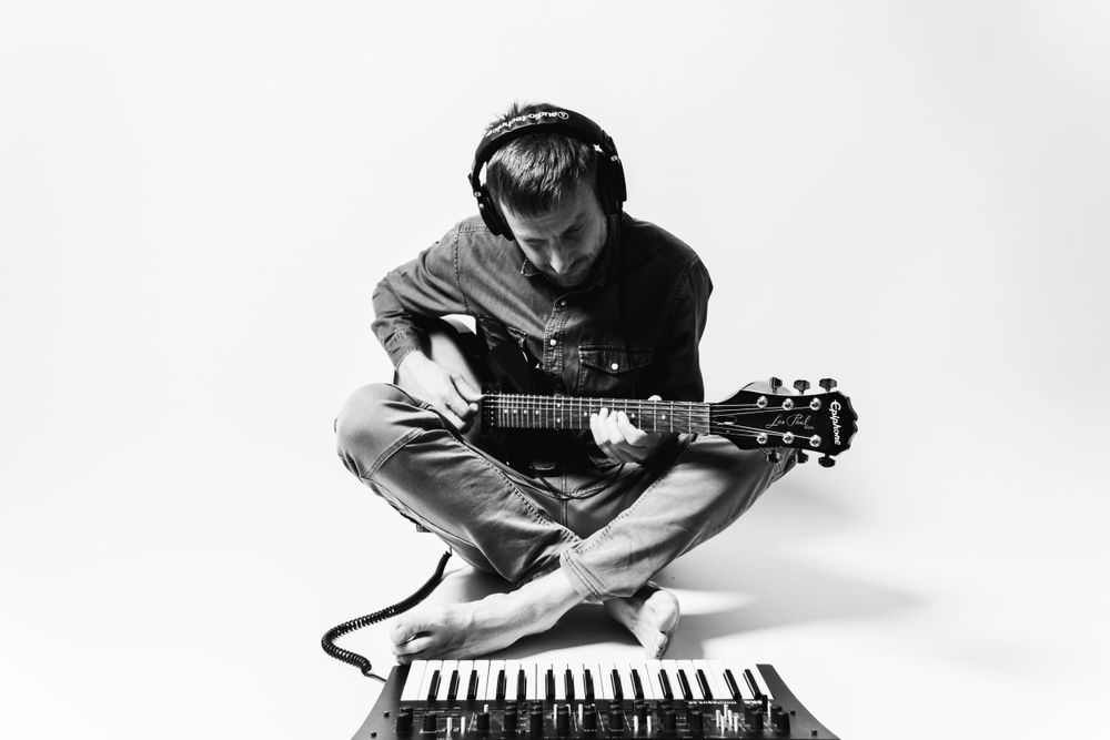 Artist performing with guitar and keyboard in studio setting.