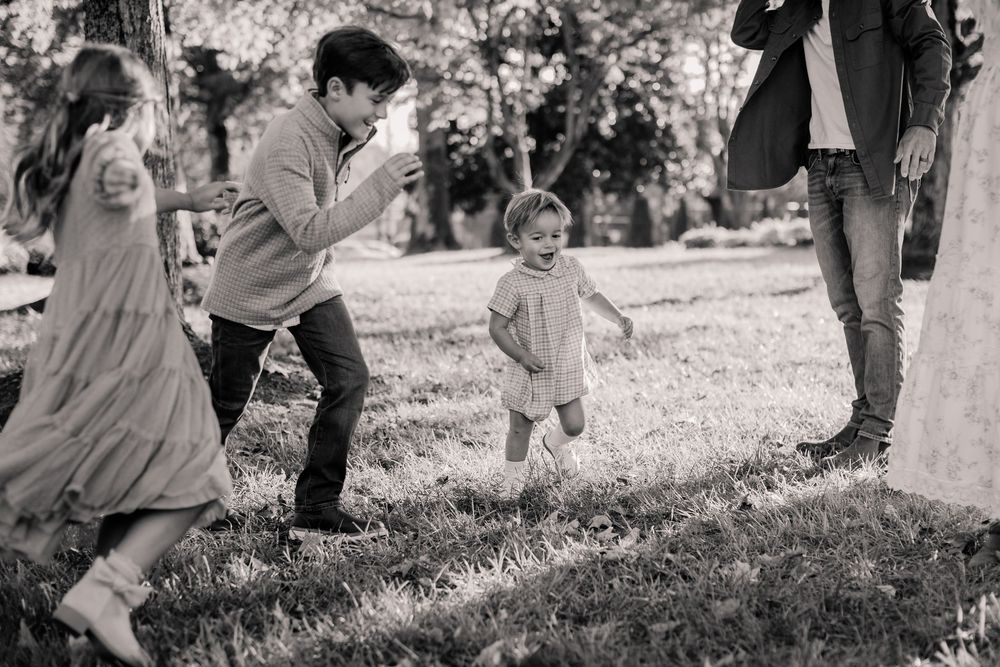 A black and white candid moment of a family playing together in a park on a sunny day.