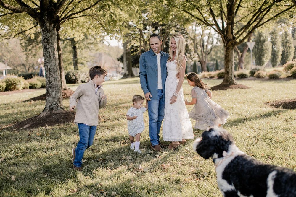 A family and their black and white dog enjoy a sunny autumn day together in a park setting with golden trees.