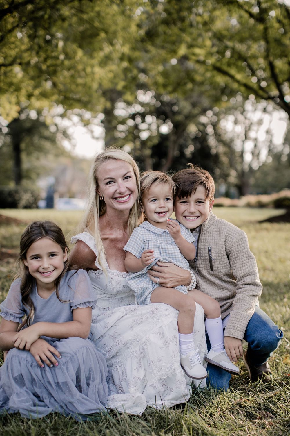 Family group sitting together on grass in matching blue and neutral tones during outdoor photo session.