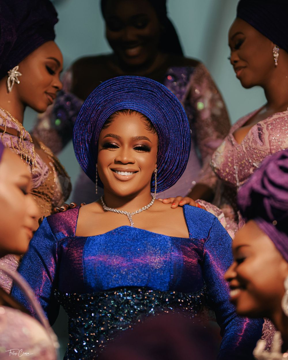 A group celebrates a festive occasion wearing traditional Nigerian attire in bright blue and pink colors.