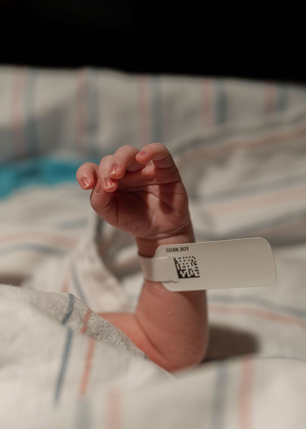 Newborn baby hand with hospital identification bracelet raised up on striped blanket.