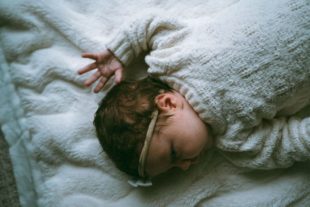 Sleeping newborn baby in white knit outfit lying on soft white blanket.