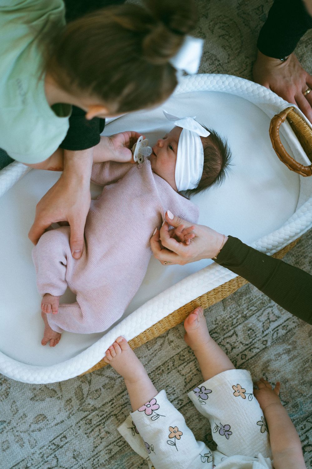 Overhead view of newborn baby in white bassinet wearing pink outfit and bow headband.