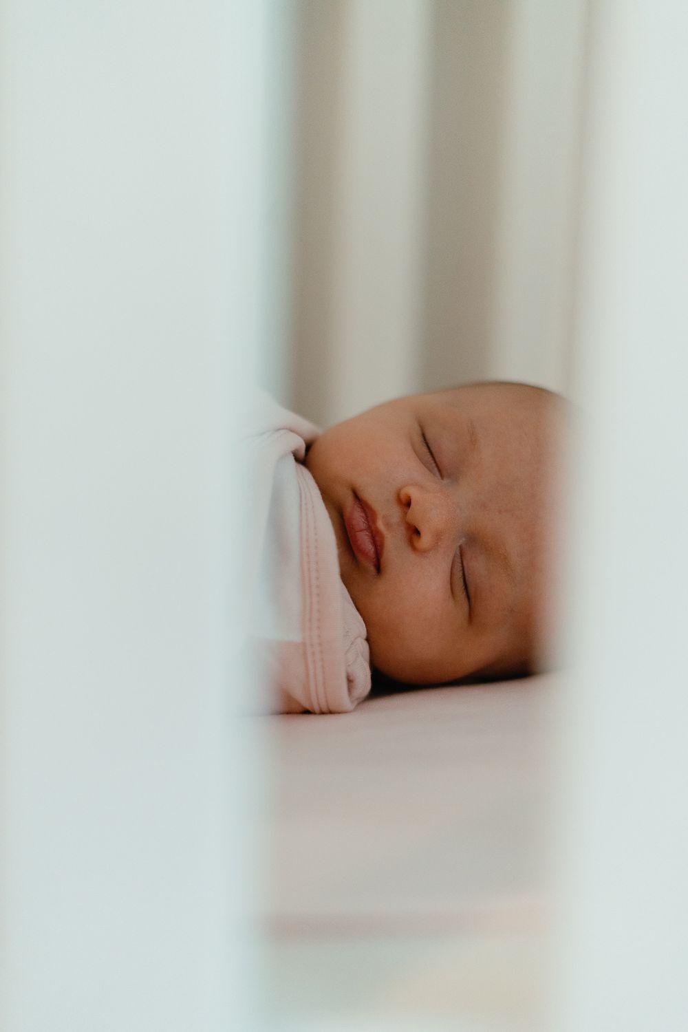 A peaceful newborn baby sleeping soundly in a white crib, wrapped in a soft pink blanket.