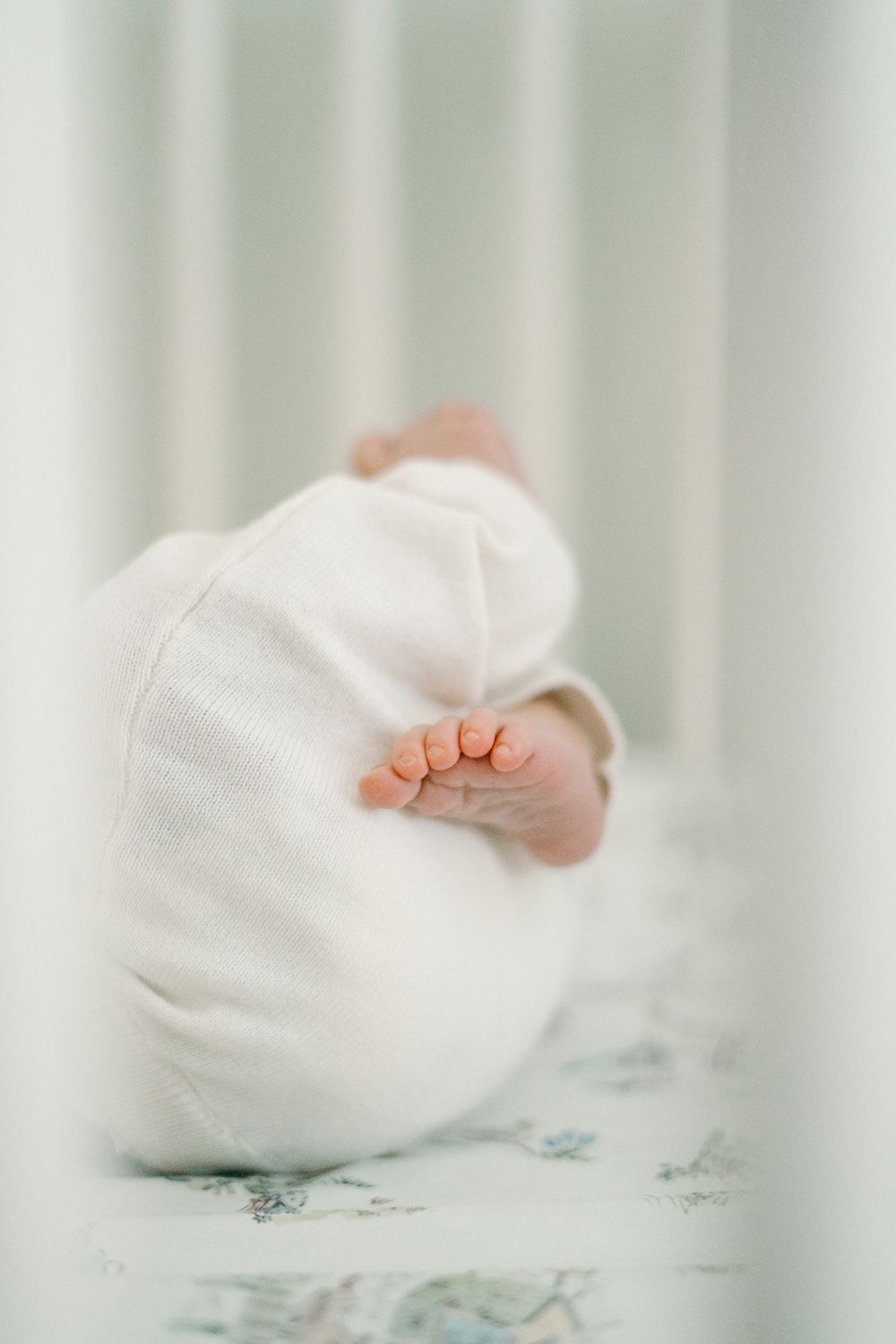 Close-up of a newborn baby's tiny feet peeking out of a white swaddle blanket in a white crib.
