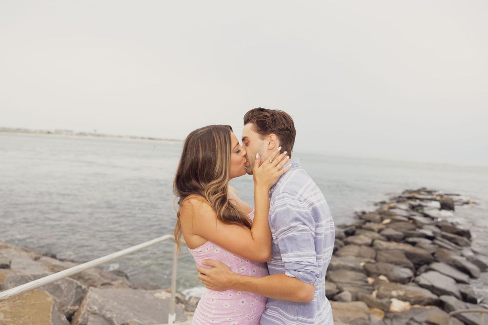 A couple embraces and kisses on a stone jetty by the sea.