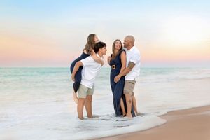 A group of people laughing together while standing in the ocean waves at sunset on a beach.