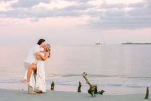 A couple shares a romantic moment on a sandy beach during sunset with the ocean waves in the background.