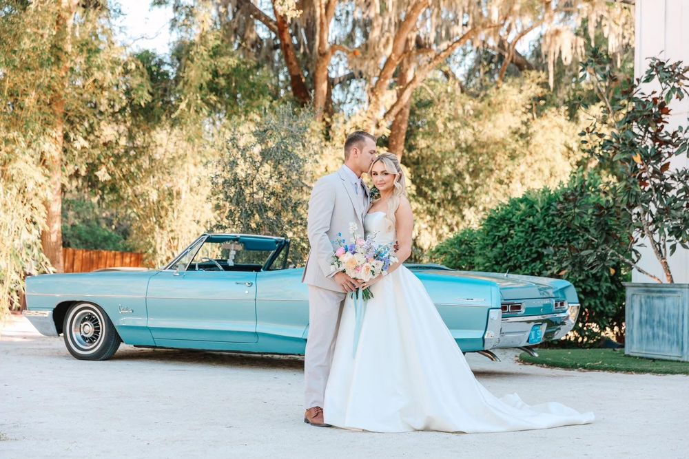 A romantic wedding photo session featuring a vintage turquoise car and flowing white dress under Spanish moss trees.