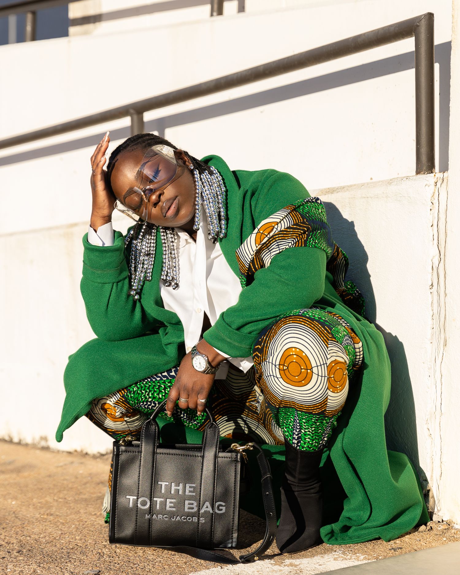 Woman in green outfit sits on tote bag outdoors, resting her head on her hand.