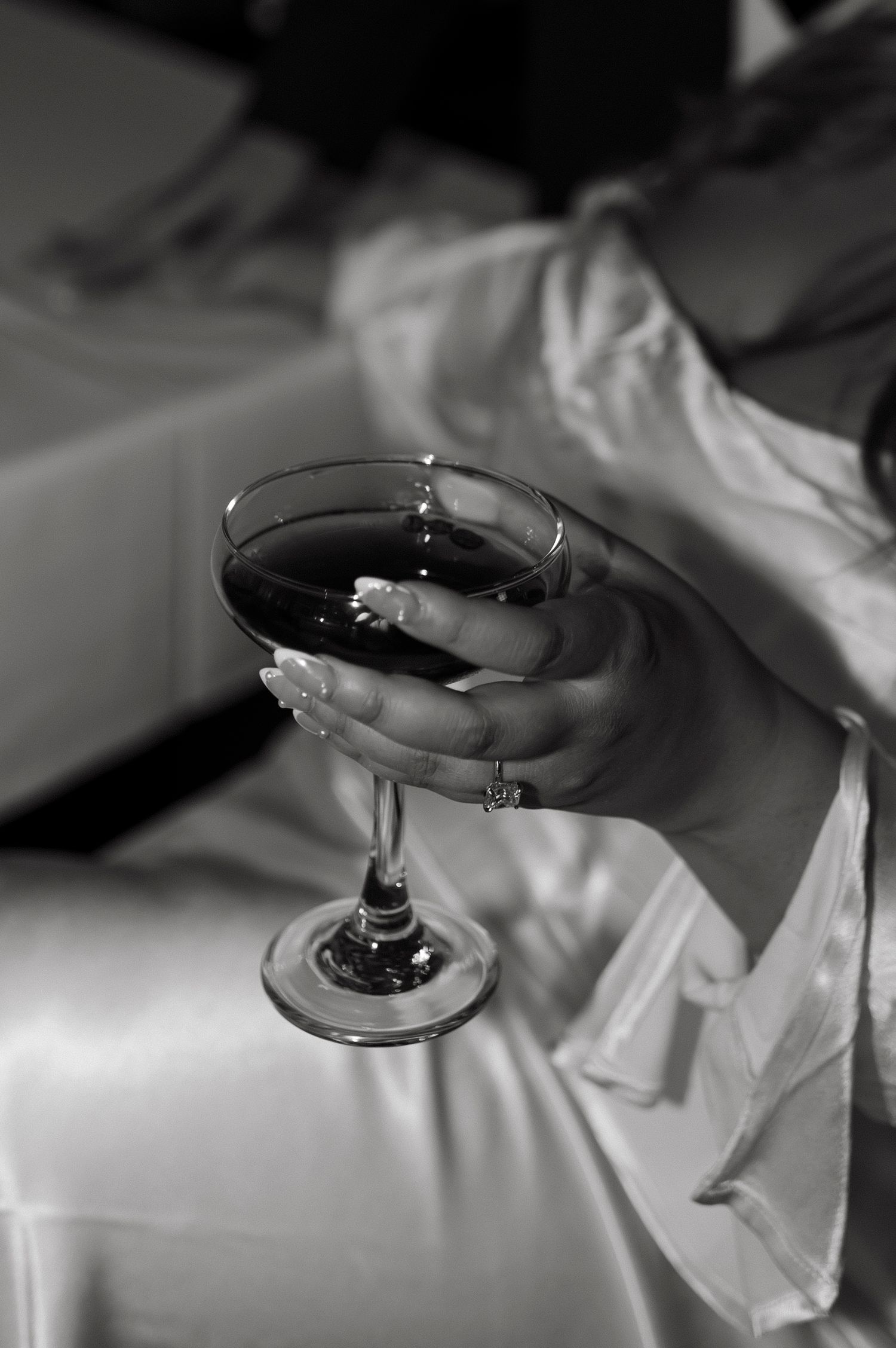 Elegant hand holding a wine glass against white fabric in black and white.