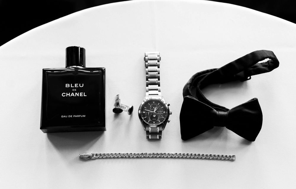 A stylish black and white flat lay composition of luxury perfume bottles, handbags, and jewelry on a light background.