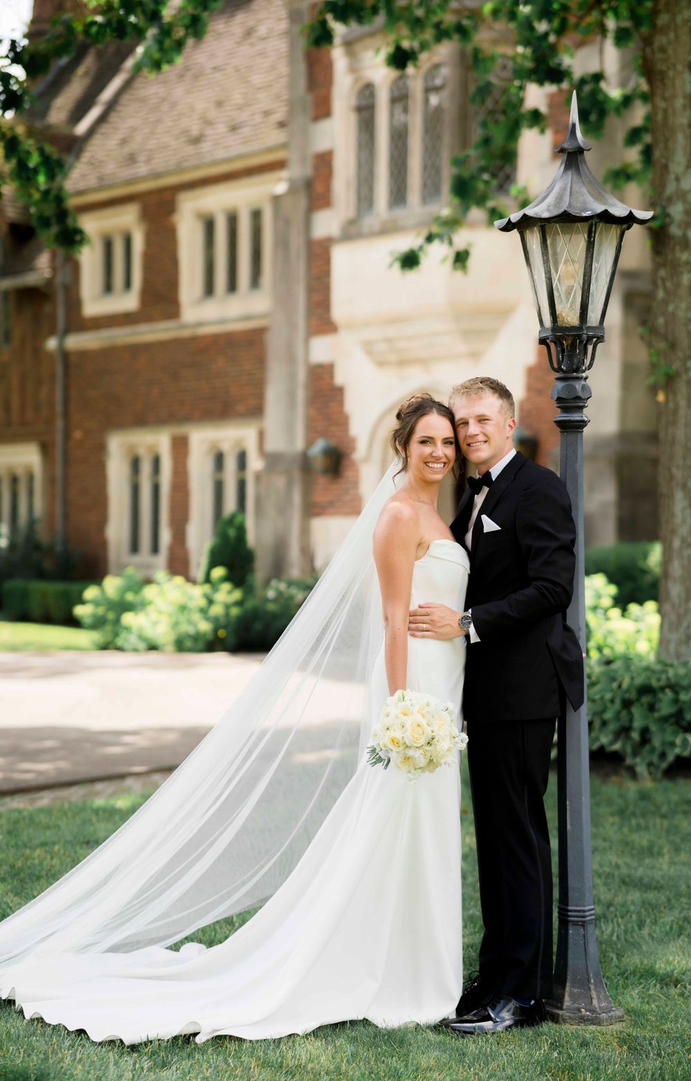Wedding couple poses for romantic portraits in front of a stone building with climbing ivy and lamp posts.