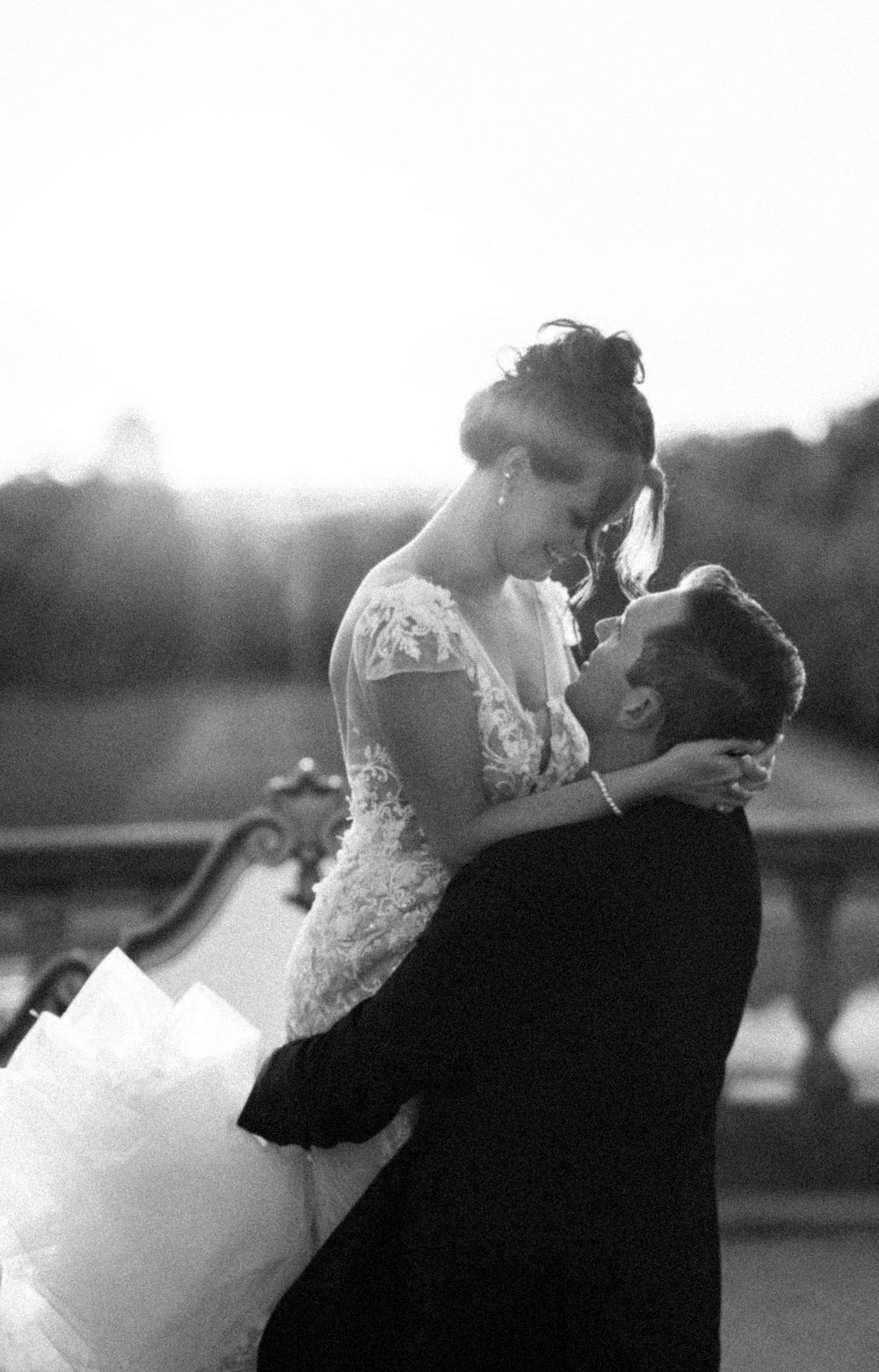 A romantic black and white wedding photo of a couple embracing at sunset, with the bride wearing a lace gown.