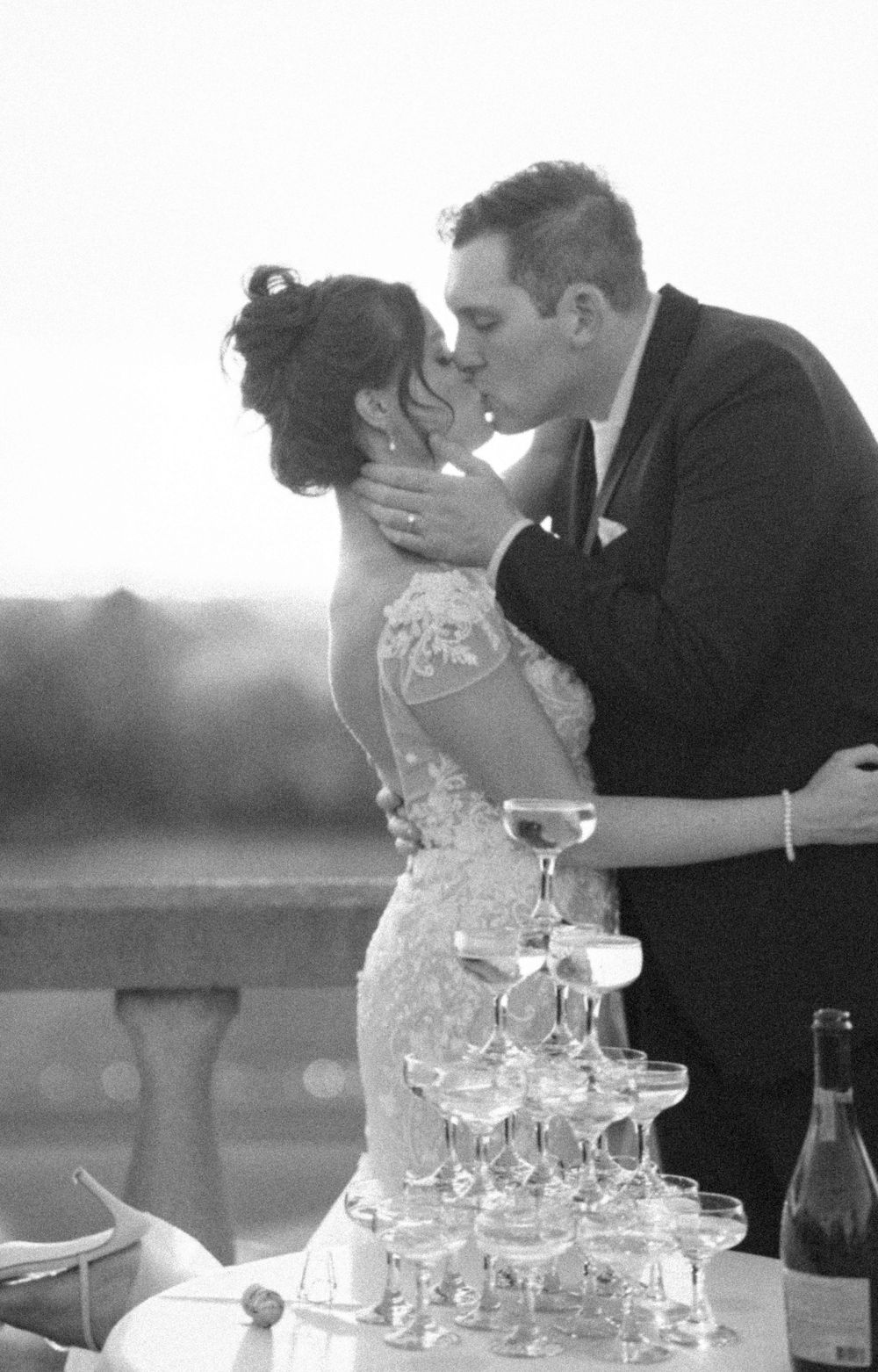Wedding couple shares romantic moment behind tower of champagne glasses at outdoor reception.