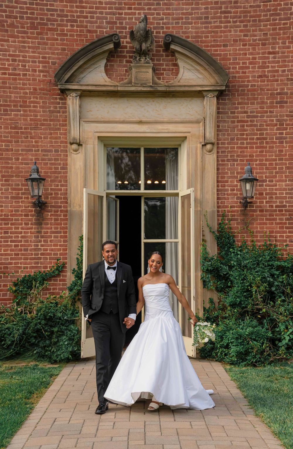 A wedding couple stands outside a stately brick building with grand doorways and stone accents.