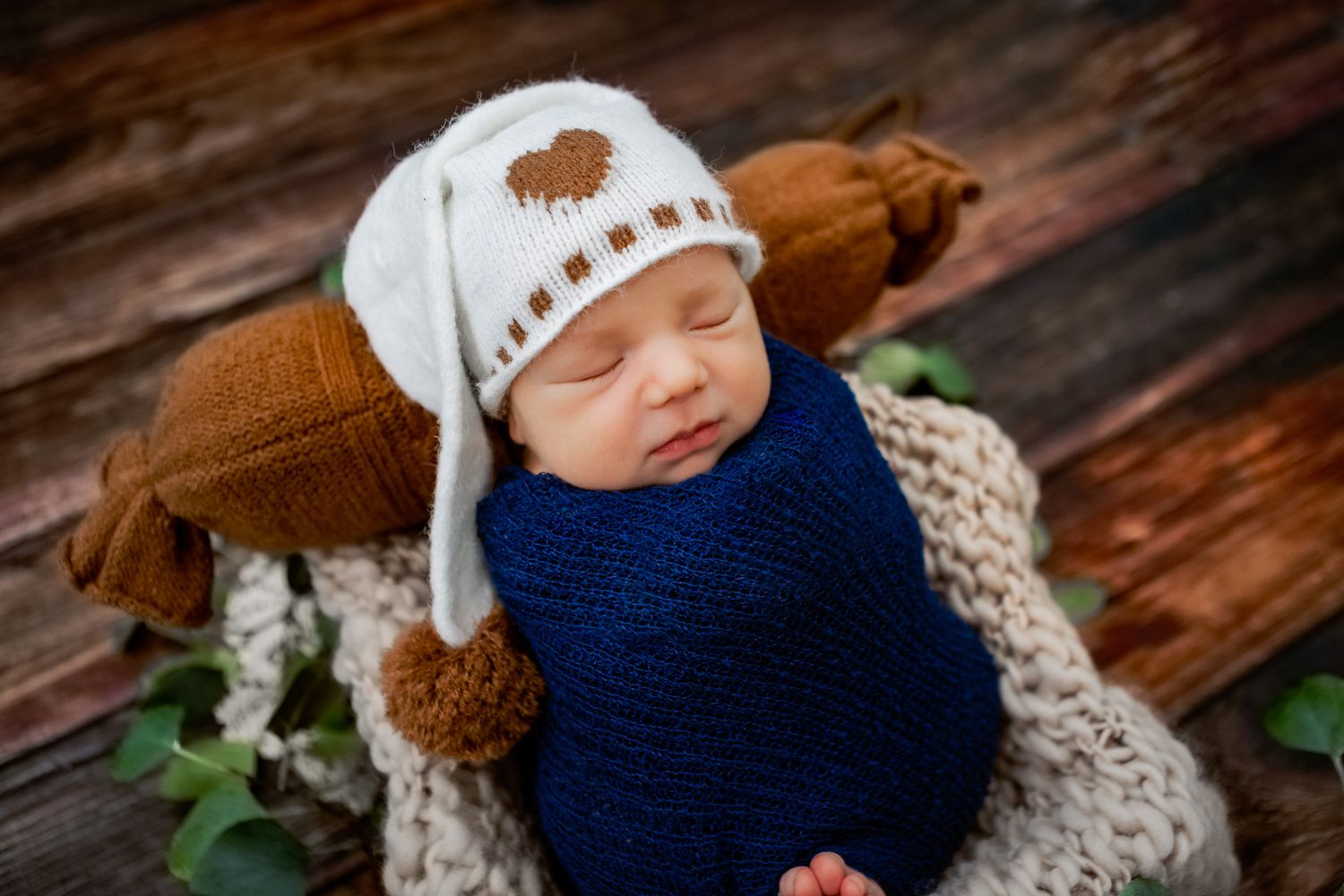 Sleeping baby during newborn session. Warm tones. Baby wearing blue wrap and brown hat. Props and backgrounds are great