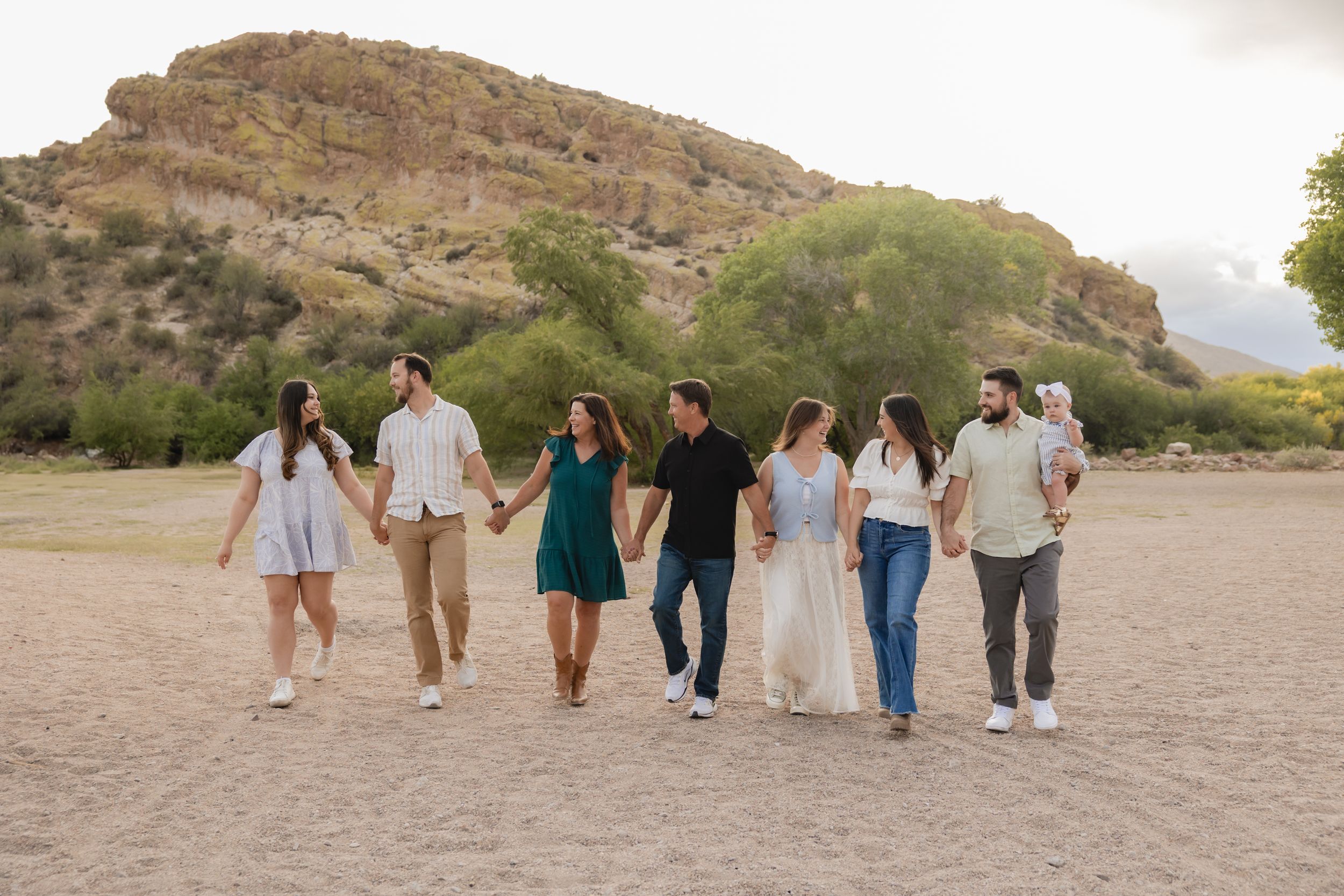 Group of people walking together at sunset on a sandy beach with rocky cliffs in the background.