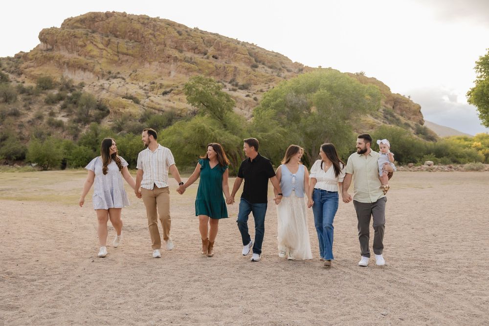 Group of people walking together at sunset on a sandy beach with rocky cliffs in the background.