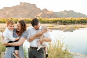 Family playing and laughing together in a serene outdoor setting with mountains and water in the background.