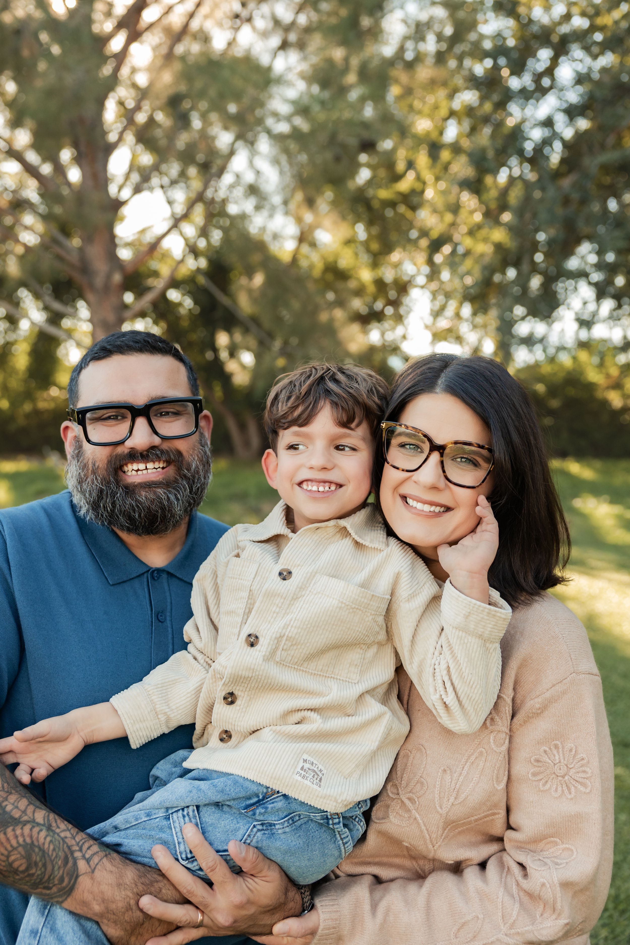A family wearing coordinated blue and beige outfits sits together outdoors during golden hour for a portrait session.