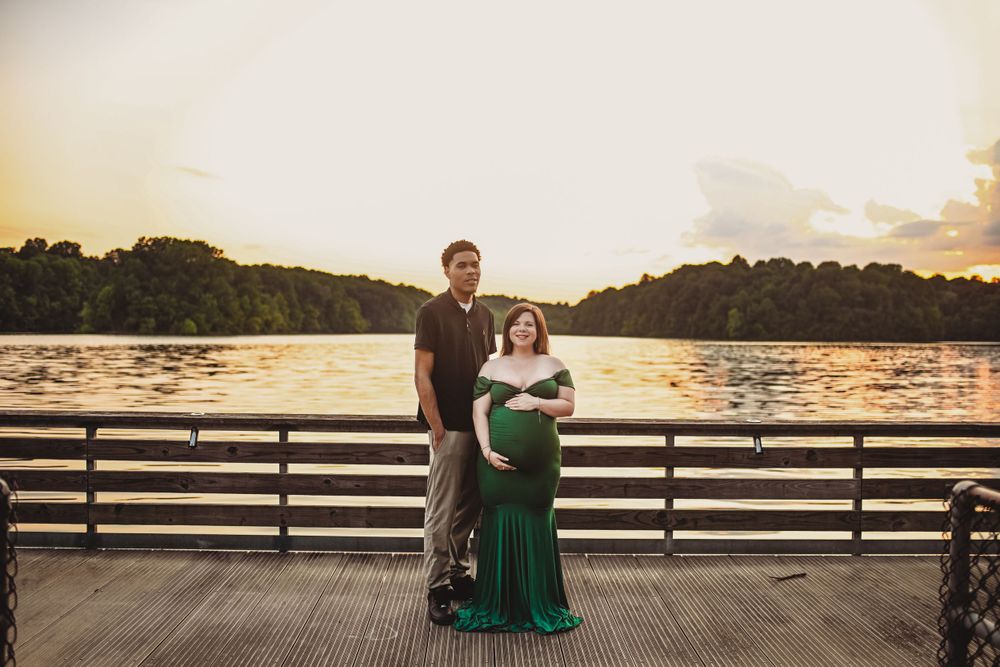 A couple poses on a wooden dock at sunset, with the woman wearing an elegant emerald green dress.