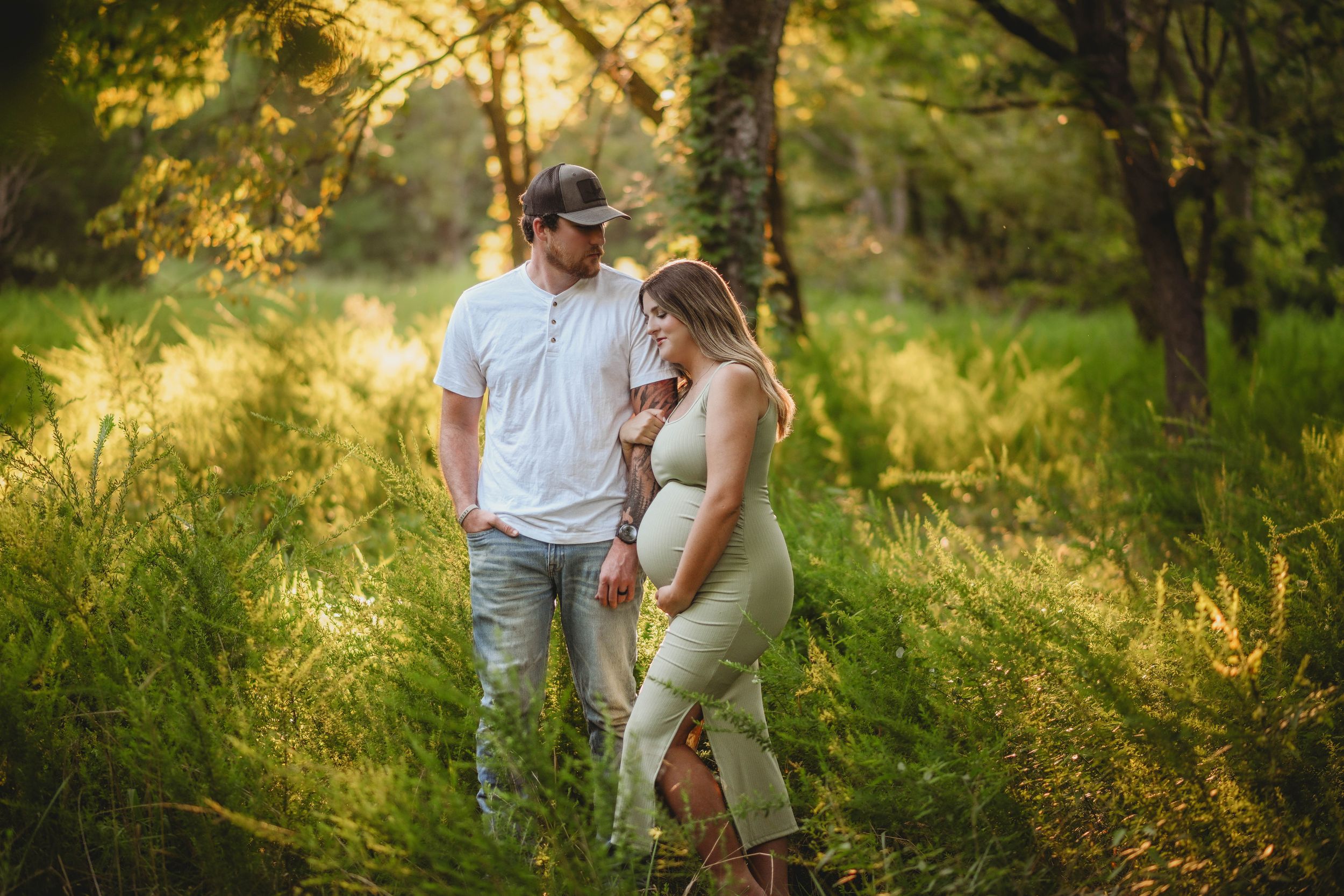 Expecting couple shares intimate moment in sunlit meadow at golden hour.