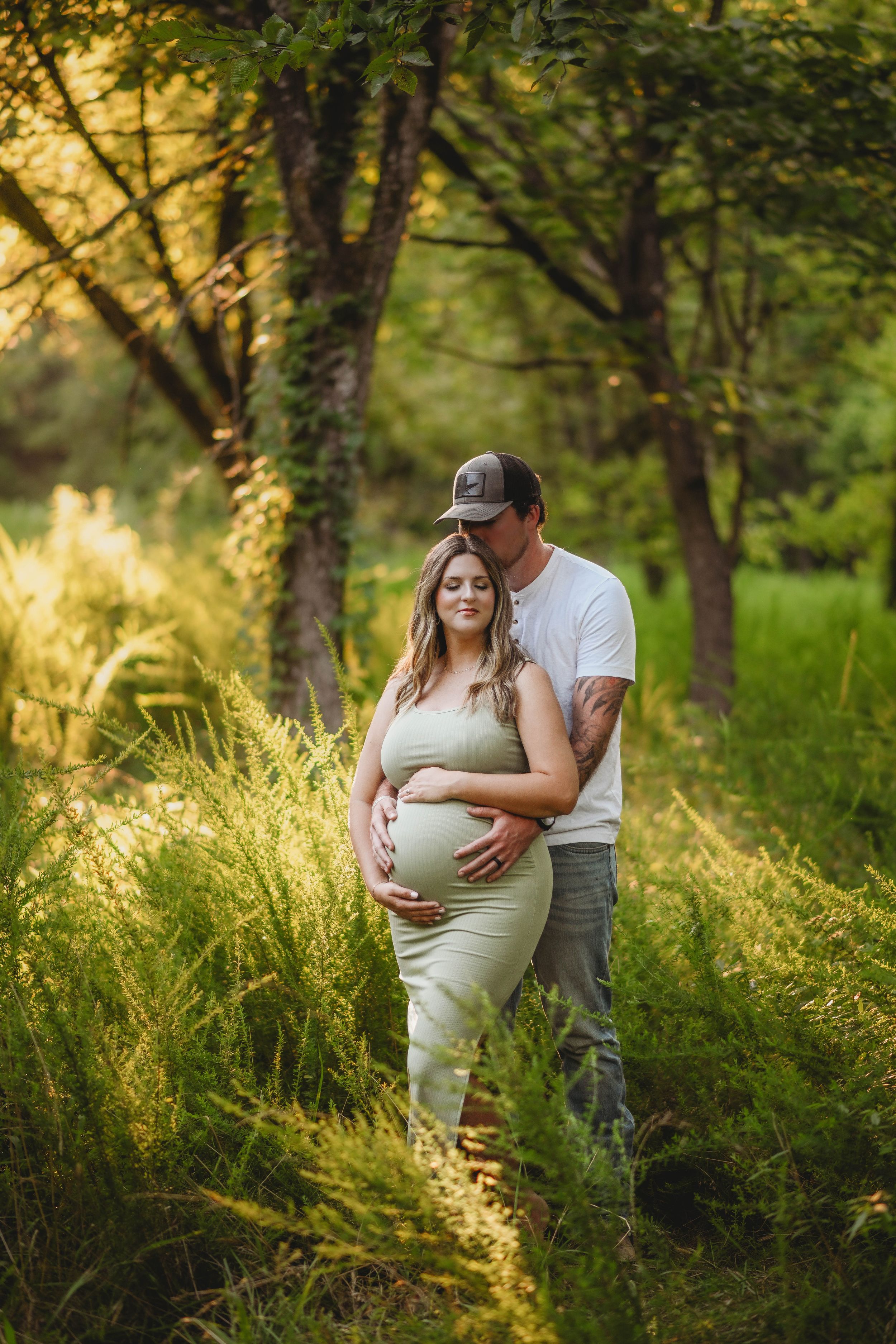 Maternity couple embracing in golden sunlit field with tall grass.