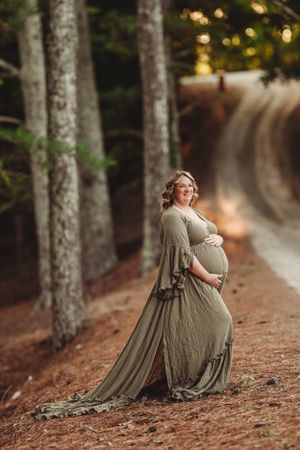 Flowing olive dress silhouette against a forest path with bokeh lighting.