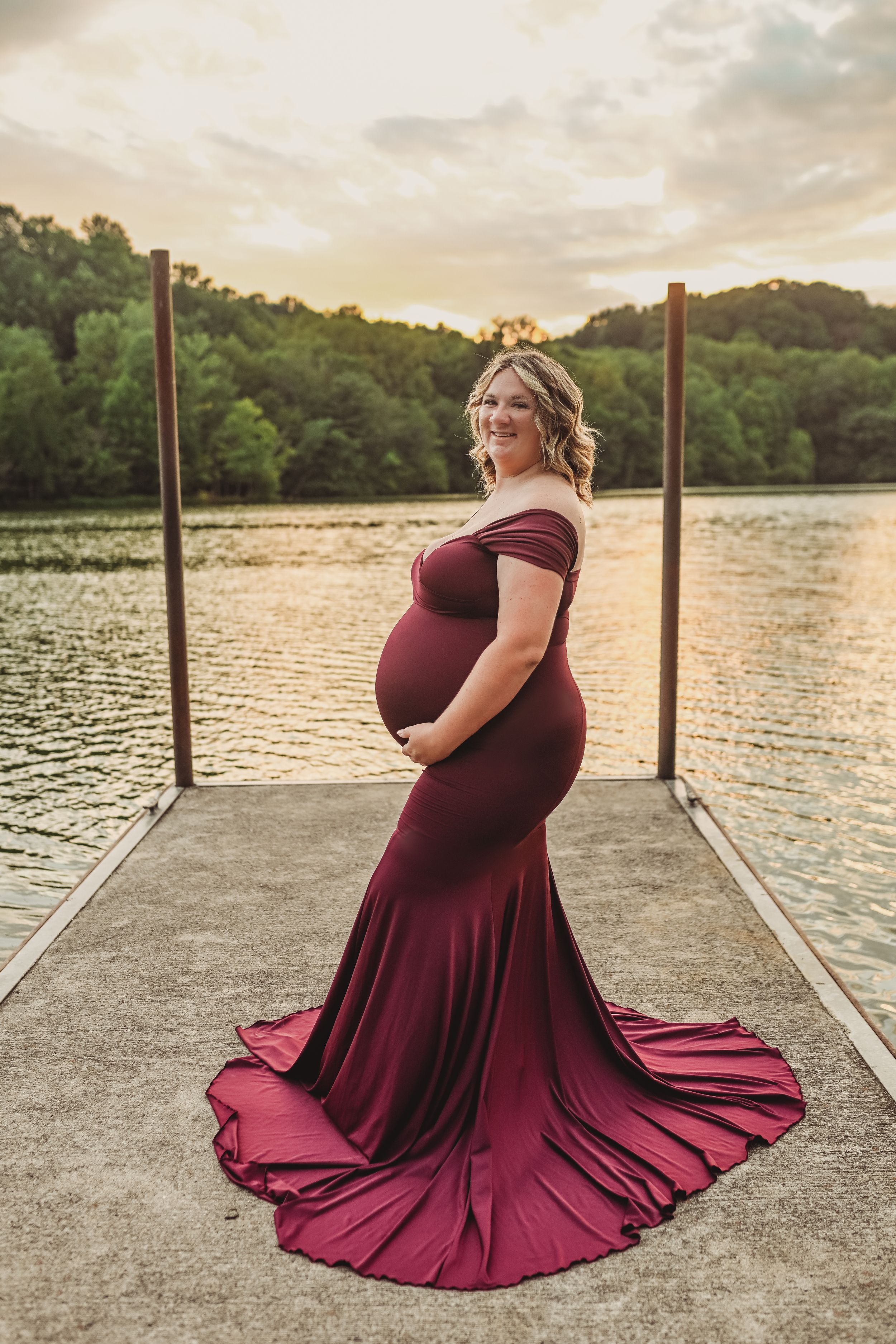 Maternity photo on a dock at sunset featuring a flowing burgundy dress.