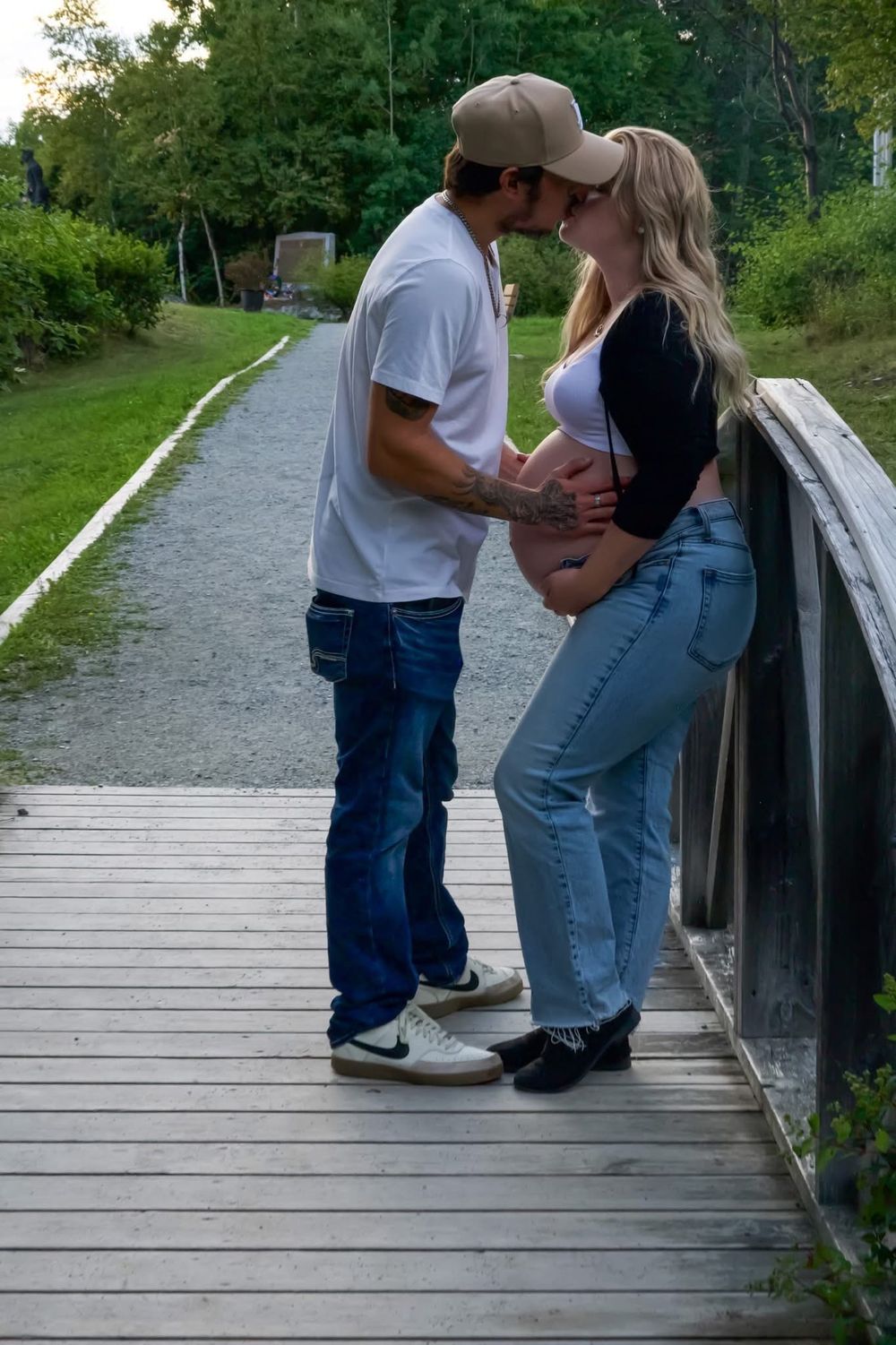 Couple sharing a kiss on a wooden bridge surrounded by lush green gardens.
