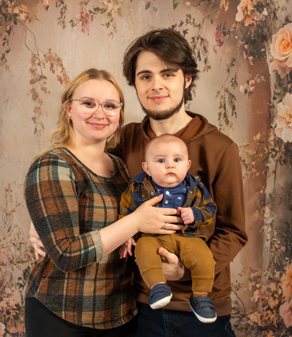 Young family portrait with mother, father, and baby in front of floral backdrop.