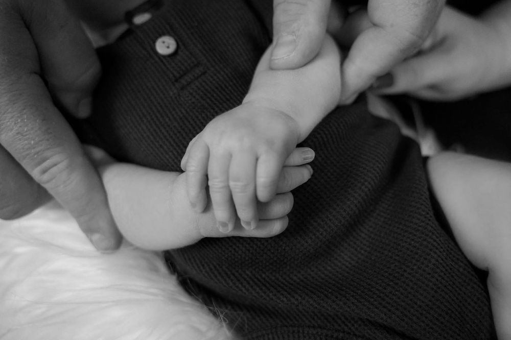 Black and white close-up of newborn baby hand grasped by parents hands.