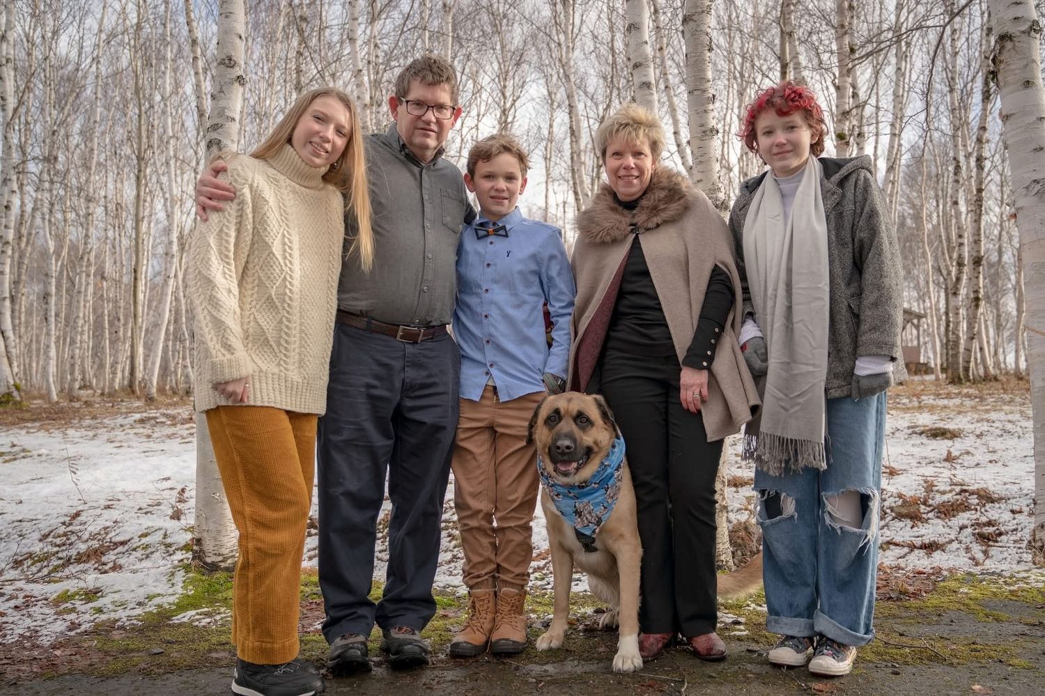 Happy family of five with dog posing outdoors among birch trees in winter portrait photo.