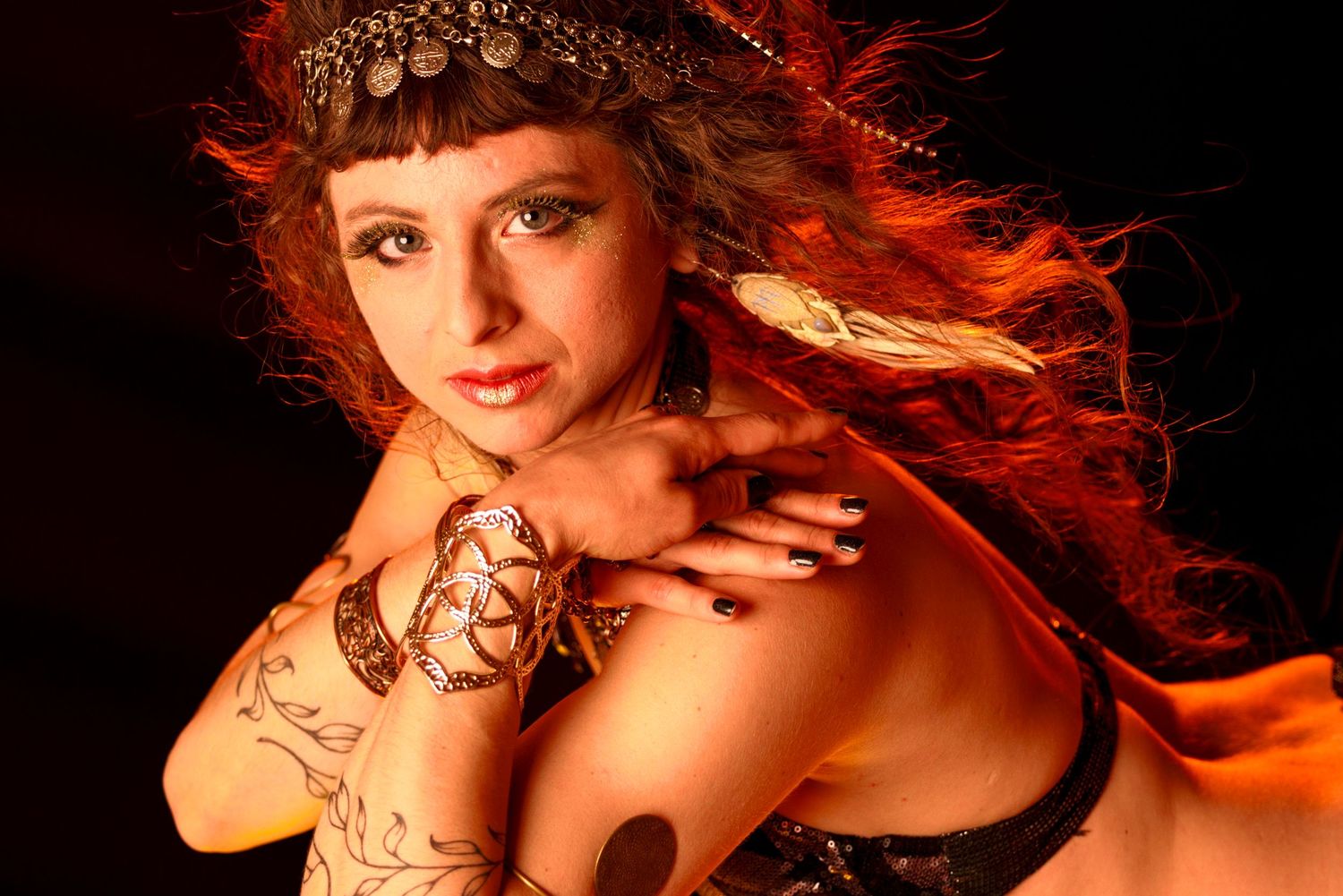 A figure with red hair and butterfly tattoos poses artistically against a dark background with dramatic lighting.