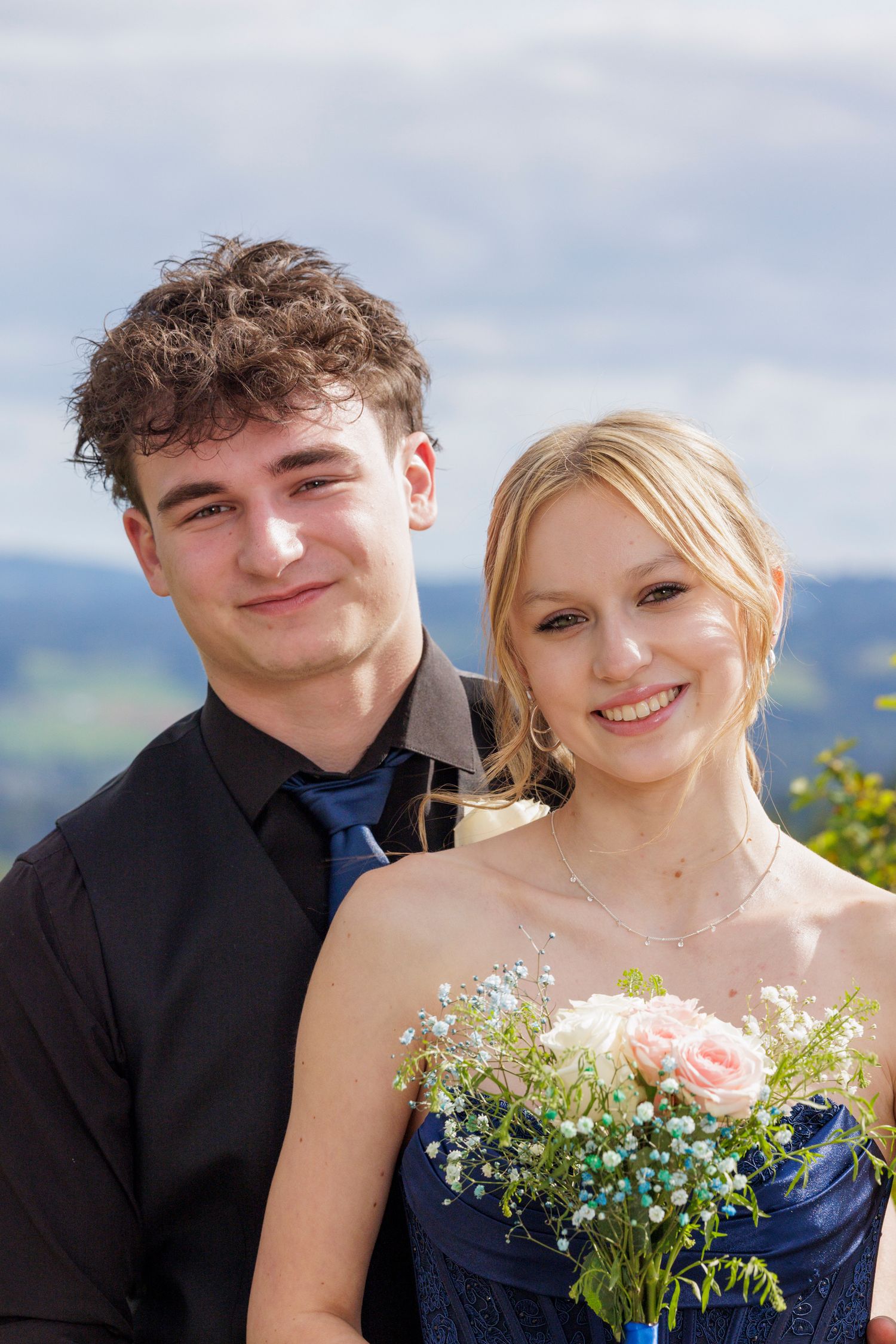 A couple shares a tender moment while dressed in formal wear against a scenic mountain backdrop.