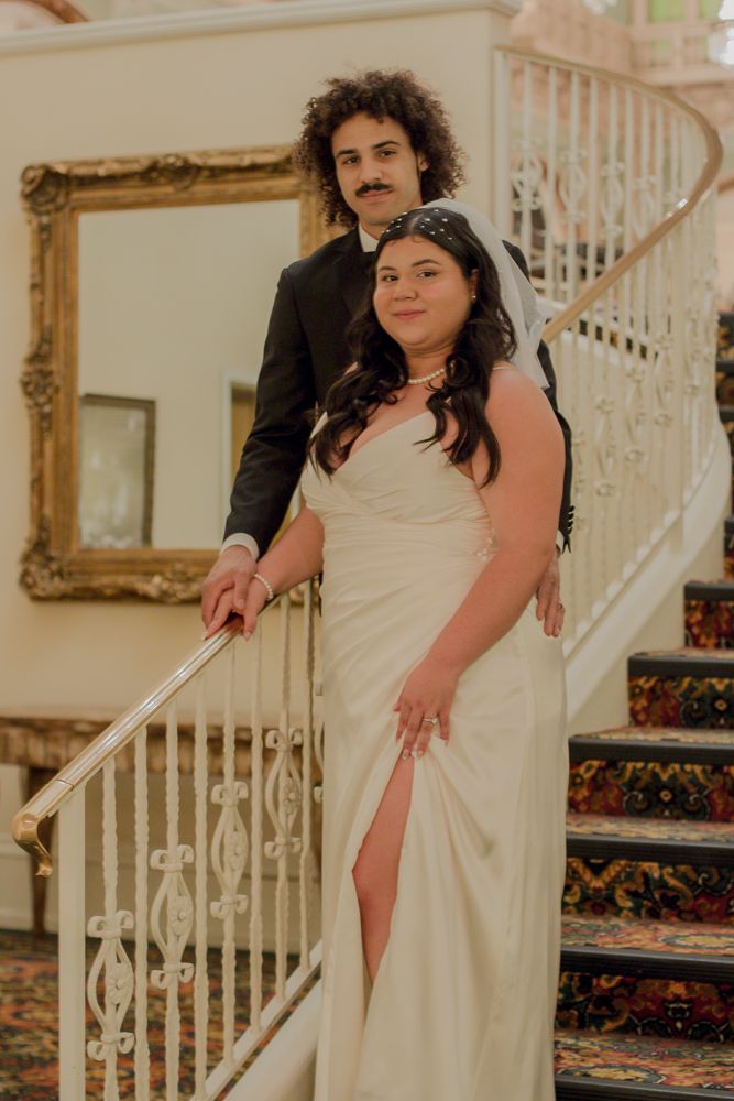 A couple poses on an elegant staircase with ornate railings during their wedding photoshoot.