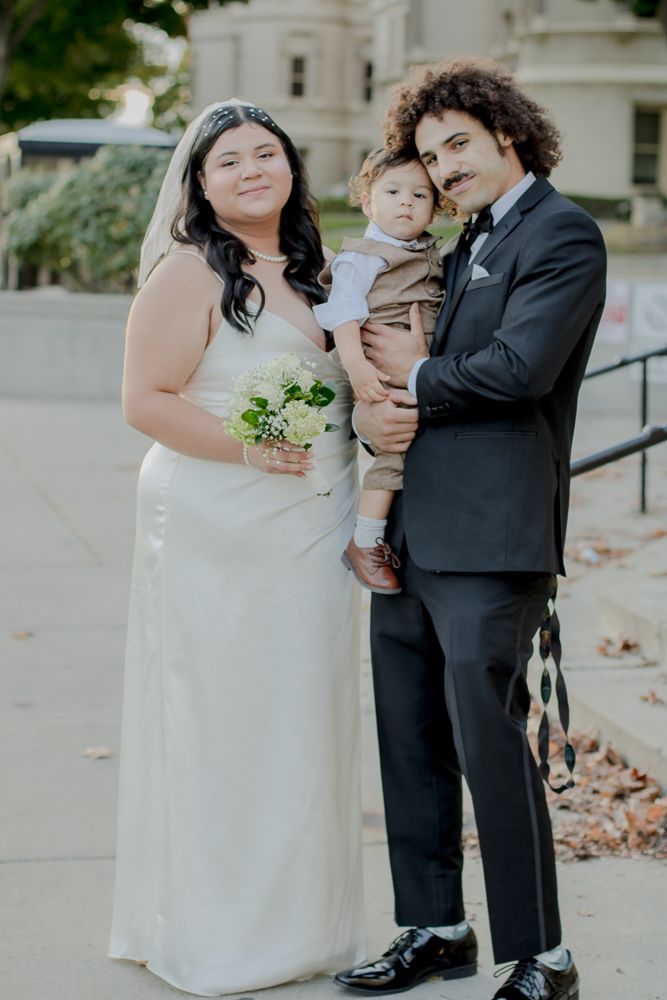 A wedding party poses outdoors with a small child in formal attire.
