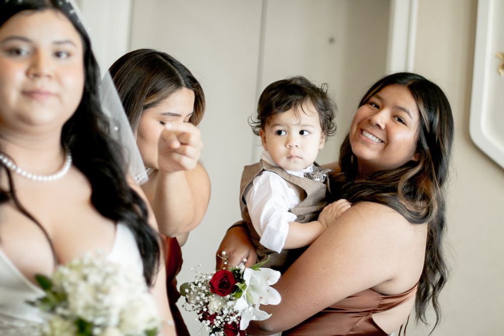 Bridesmaids in burgundy dresses share joyful moments while holding a small child at a wedding celebration.